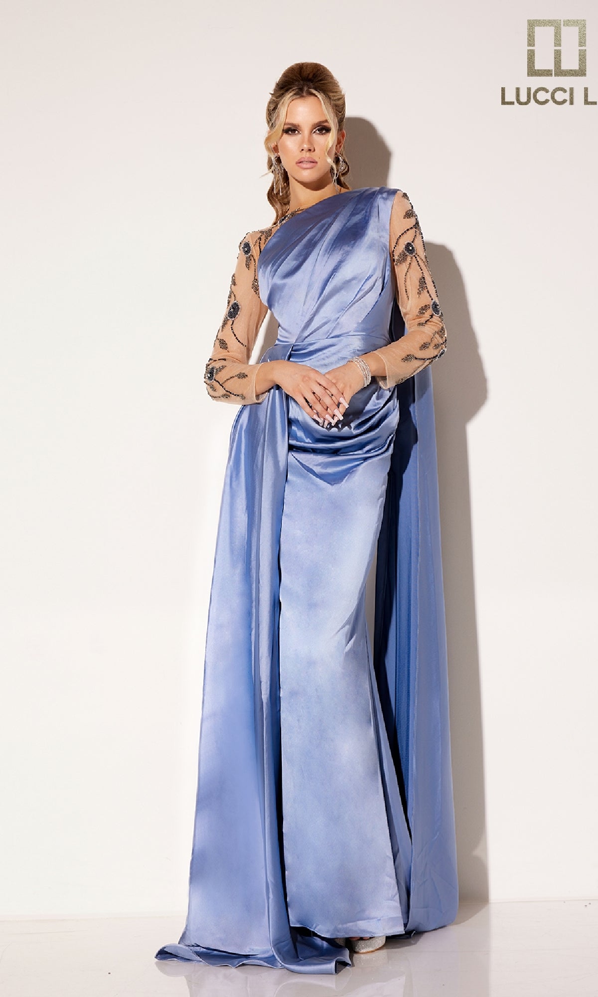 A woman wearing the Lucci Lu C8066, a long formal dress in periwinkle blue with sheer, floral-beaded sleeves, stands against a plain light background.